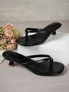 Élégantes sandales à petit talon noires sur support blanc et fond fleuri