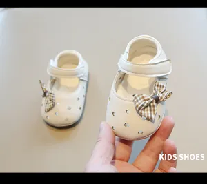 Detalle de los zapatos de bebé blancos con diseño calado y lazo decorativo de cuadros
