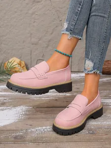 Close-up of pink frosted leather loafers with thick soles on rustic wooden floor