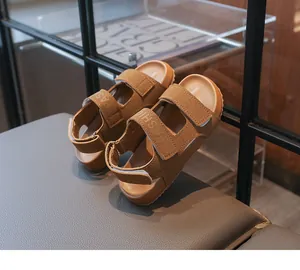 Stilvolle braune Kindersandalen mit offener Spitze auf einem modernen Glasregal präsentiert.