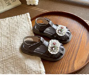 Detailed macro shot of children's brown closed-toe sandals featuring elegant lace floral accents