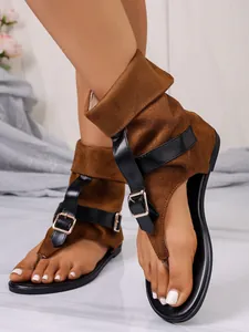 Detalle de sandalias de gamuza marrón con tiras negras y hebilla dorada en el tobillo.