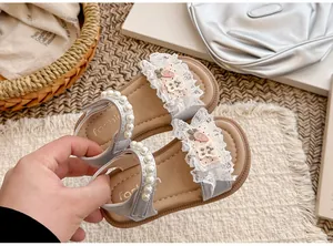 Detailansicht der silbernen Mädchensandalen mit Perlenriemen, Spitzenrüschen und Patches