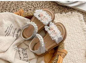 Detailansicht von Mädchensandalen mit Perlenriemen und zarten Spitzenrüschen.