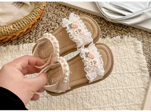 Nahaufnahme von niedlichen rosafarbenen Mädchensandalen mit Spitzenrüschen und Perlenriemen