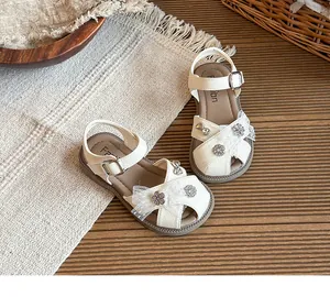 Detailed view of girls' white hollow-out sandals with lace bow and rhinestones