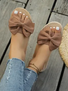 Dettaglio di ciabatte estive piatte con grande fiocco in tessuto su legno