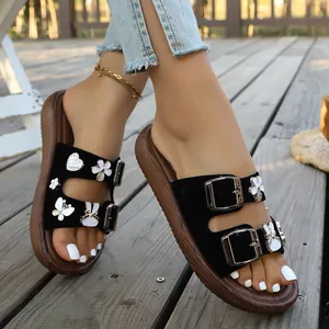 Nahaufnahme schwarzer Plateausandalen mit Herz-Strass und Schmetterlingsanhängern