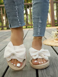 Dettaglio ciabatte beige con grandi fiocchi in tessuto e trama intrecciata su legno