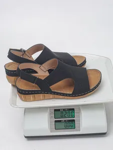 Vista dettagliata di leggeri sandali neri con zeppa su una bilancia digitale che pesano 0,2 kg.