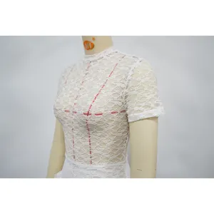 Dettaglio ravvicinato dell'intricato motivo in pizzo floreale bianco sul body a collo alto