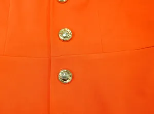Close-up detail van levendig oranje stof en gouden decoratieve knopen op een jumpsuit.