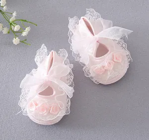 Detailed view of pink baby pre-walker shoes with lace trim and fabric rose flowers.