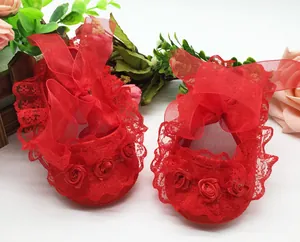 Close-up detail showing red baby pre-walker shoes with lace trim and ribbon flowers