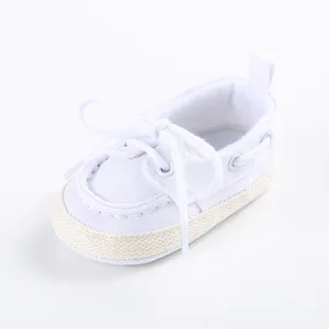 Dettaglio scarpe neonato in tela bianca con suola morbida per bambini 0-1 anni.