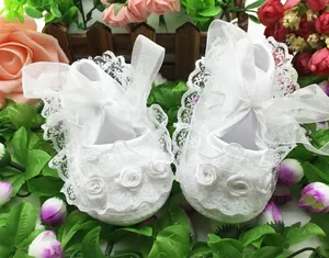 Close-up of elegant white lace infant walking shoes featuring decorative silk roses and soft soles