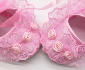 Close-up detail of pink baby walker shoes with delicate floral lace and rose buds.