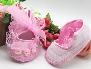 Detailed view of pink lace baby shoes featuring decorative ribbons and small rose flowers.