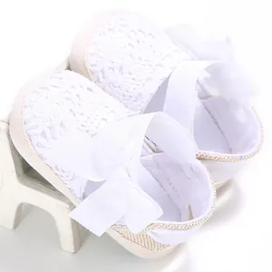 Close-up view of white hollow-out crochet baby shoes with elegant ribbon bow detail.