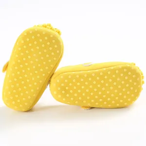 Detalle de zapatos amarillos para bebé con suelas suaves y puntos antideslizantes.