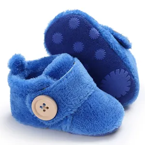 Close-up of blue plush baby shoes with decorative wood button and non-slip sole.