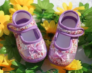 Primer plano de zapatos para bebé con flores moradas, lazos de cinta y suelas de tela suave