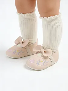 Detail view of pink embroidered baby princess shoes featuring a bow and cream ribbed socks.