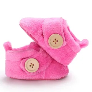 Close-up of pink fuzzy baby booties with a decorative wooden button and soft fleece.