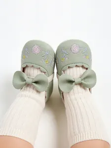 Close-up of sage green embroidered baby shoes with bow and ribbed socks.