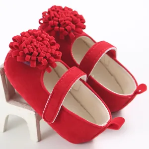 Primer plano de zapatos de princesa para bebé en terciopelo rojo con grandes pompones.