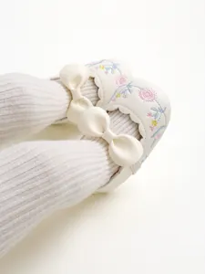 Close-up of vintage white baby shoes with delicate floral embroidery and bow