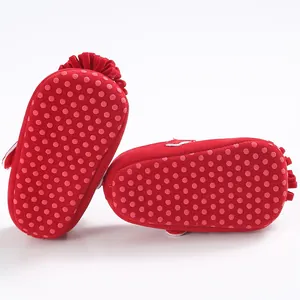 Detalle de suelas antideslizantes con puntos de goma en zapatos rojos de bebé estilo princesa.