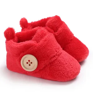 Soft red plush baby booties with a large decorative wooden button and cozy fuzzy texture.
