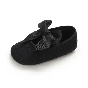 Détail de chaussure de marche bébé en dentelle noire avec un nœud en ruban décoratif.