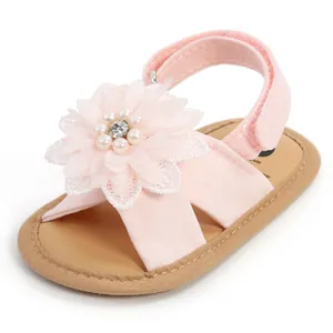 Détail d'une sandale rose pour bébé avec une fleur en dentelle, perles et strass.