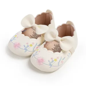 Detail view of cream baby shoes with floral embroidery and a large decorative bow