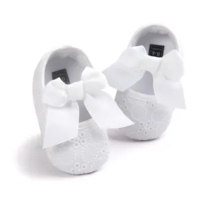 Close-up of white embroidered infant princess shoes with large bows for 0-6 months.