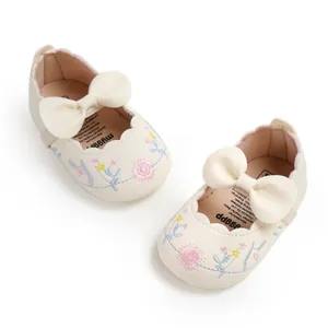 Close-up detail of embroidered flower pattern and bow on cream baby princess shoes