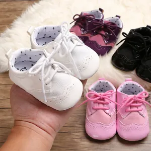 Detail view of soft-sole white baby pre-walker shoes held by hand among pink and purple pairs