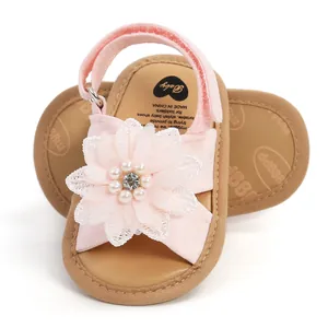 Détail de sandales roses pour bébé avec une grande fleur de perles et des semelles souples.