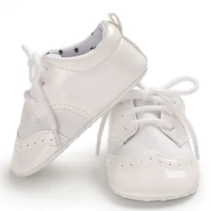 Close-up detail of white patent leather baby pre-walker shoes with elegant lace-up design