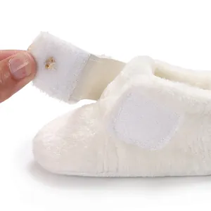 Close-up view of the adjustable hook-and-loop strap on soft white plush baby walking shoes.