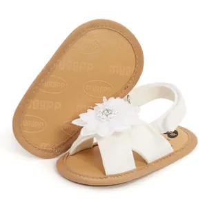 Gros plan sur des sandales blanches pour bébé avec une fleur en tissu et des perles.