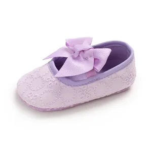 Détail d'une chaussure de bébé violette avec dentelle florale et grand nœud ruban