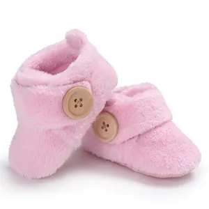 Soft pink plush baby booties featuring decorative wooden buttons and fuzzy pom-poms