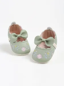 Close-up of sage green baby princess shoes featuring delicate floral embroidery and a large bow