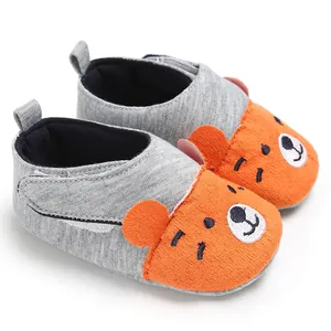 Gros plan de jolies chaussures pour bébé ours orange avec semelles souples et tissu gris.