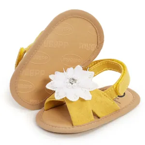 Gros plan de sandales jaunes pour bébé avec fleur en perles blanches et semelles souples.