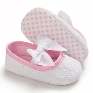 Gros plan de chaussures de princesse pour bébé en dentelle blanche avec semelles roses à pois.