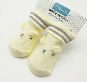 Detail of pale yellow baby socks with 3D bear ears and striped cuffs on packaging